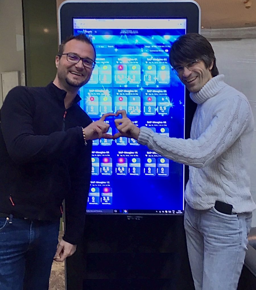 Deux membres de l’équipe ChargeAngels formant un cœur avec leurs mains devant le tableau de bord ChargeAngels affiché sur un grand écran tactile